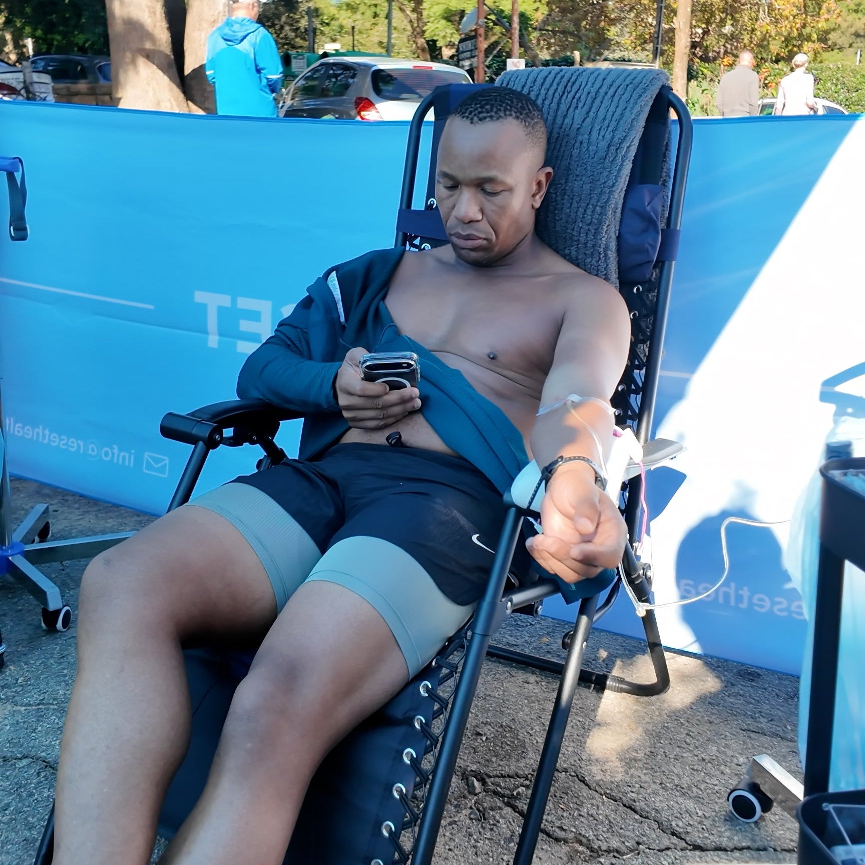 Man sitting in a folding chair using a phone with a blue backdrop and 'T3' branding.